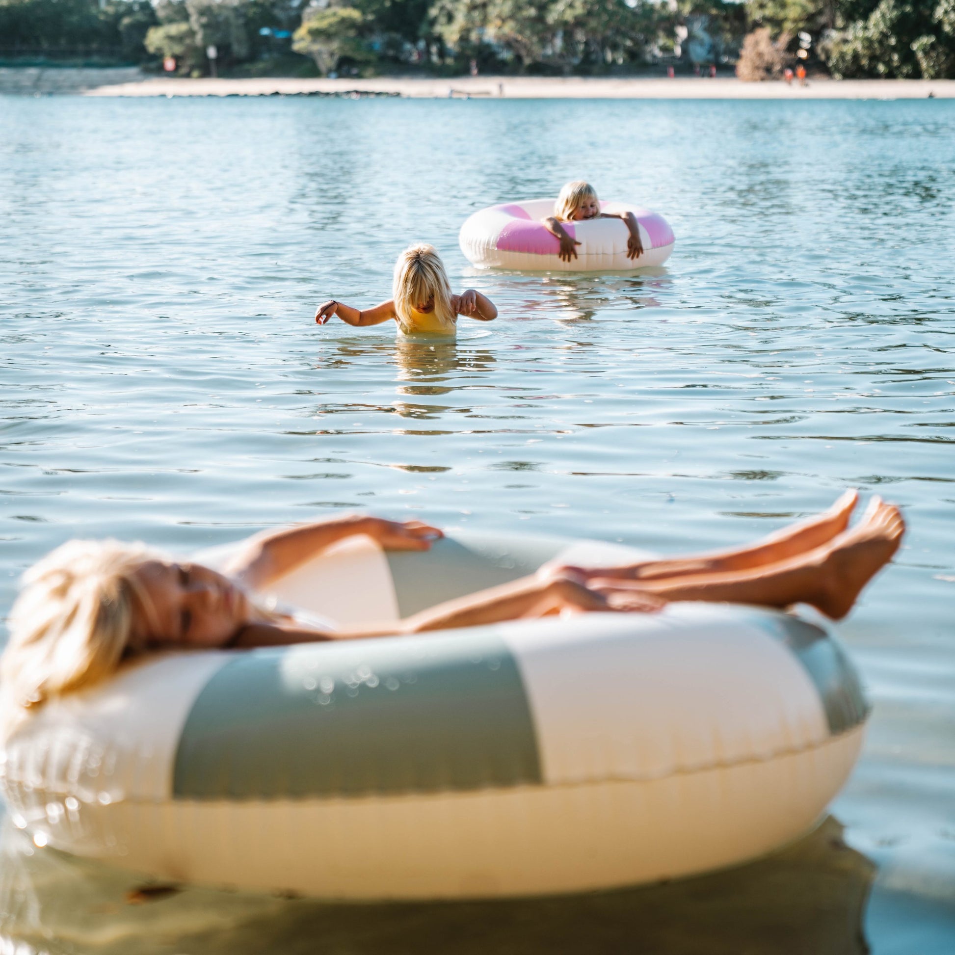 Koło do pływania dla dorosłych marki SUNNY LIFE używane przez osoby na jeziorze podczas słonecznego dnia