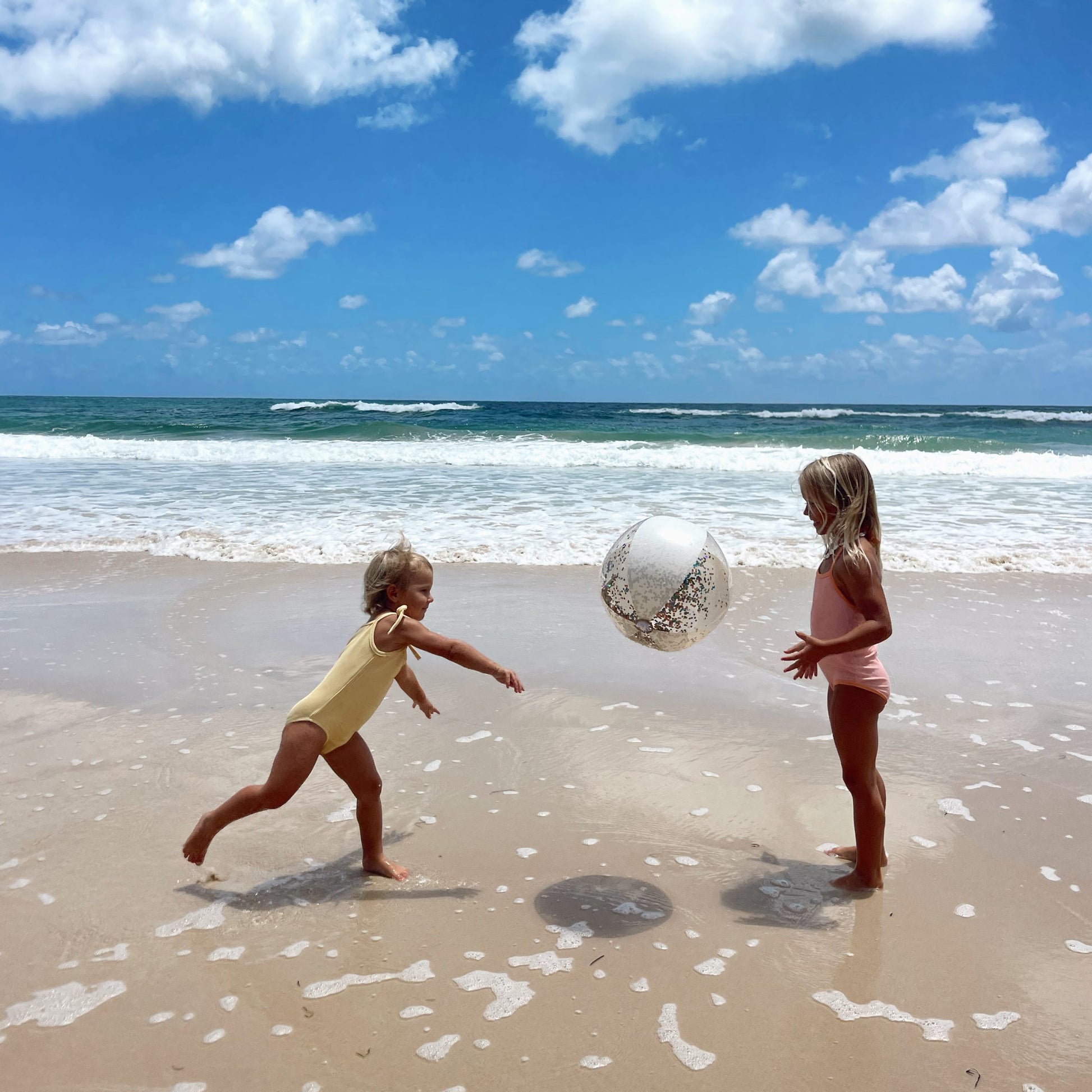 Dwie dziewczynki bawiące się nadmuchiwaną piłką plażową z brokatem na piaszczystej plaży przy oceanie