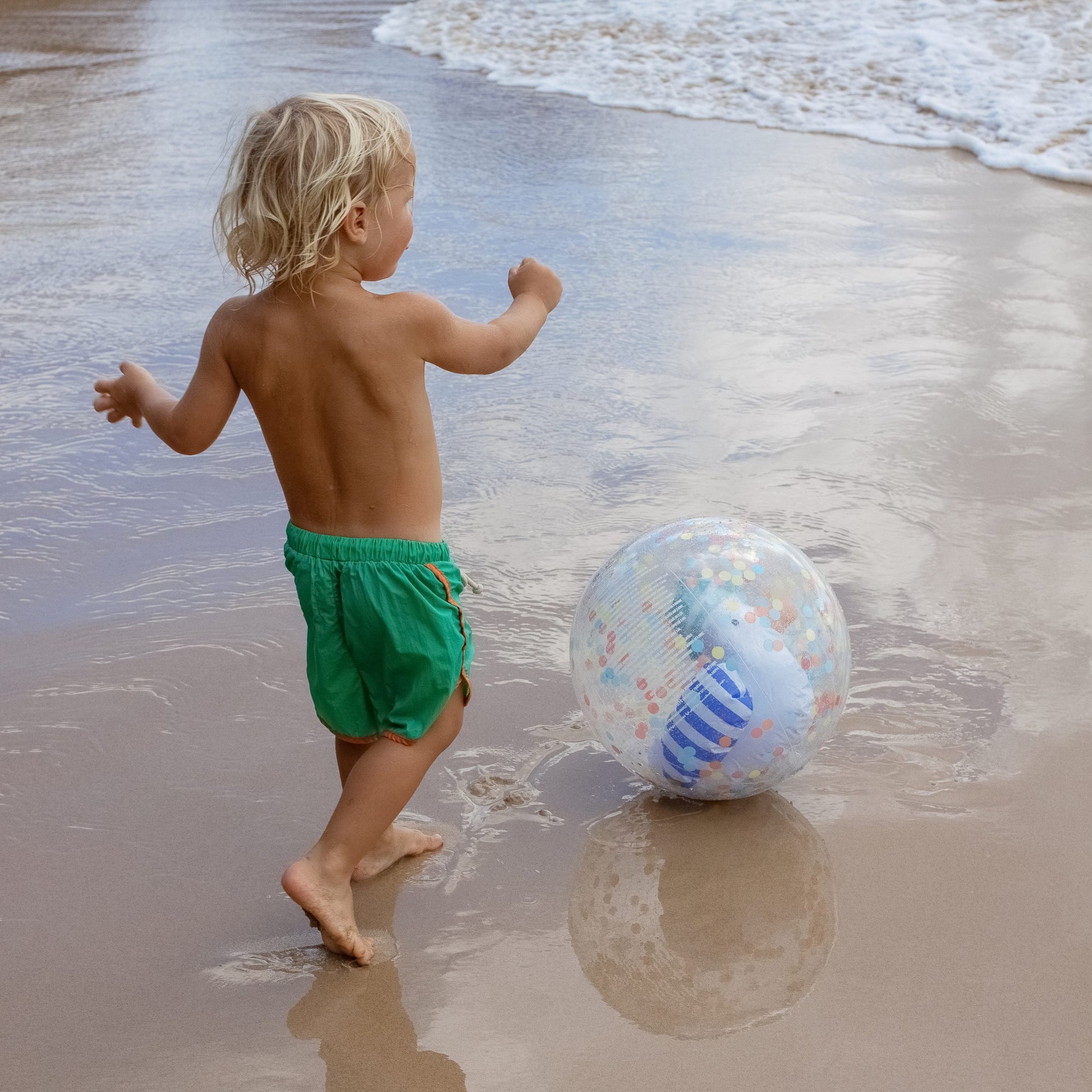 Dziecko bawiące się nadmuchiwaną piłką plażową dla dzieci na piaszczystej plaży przy falach