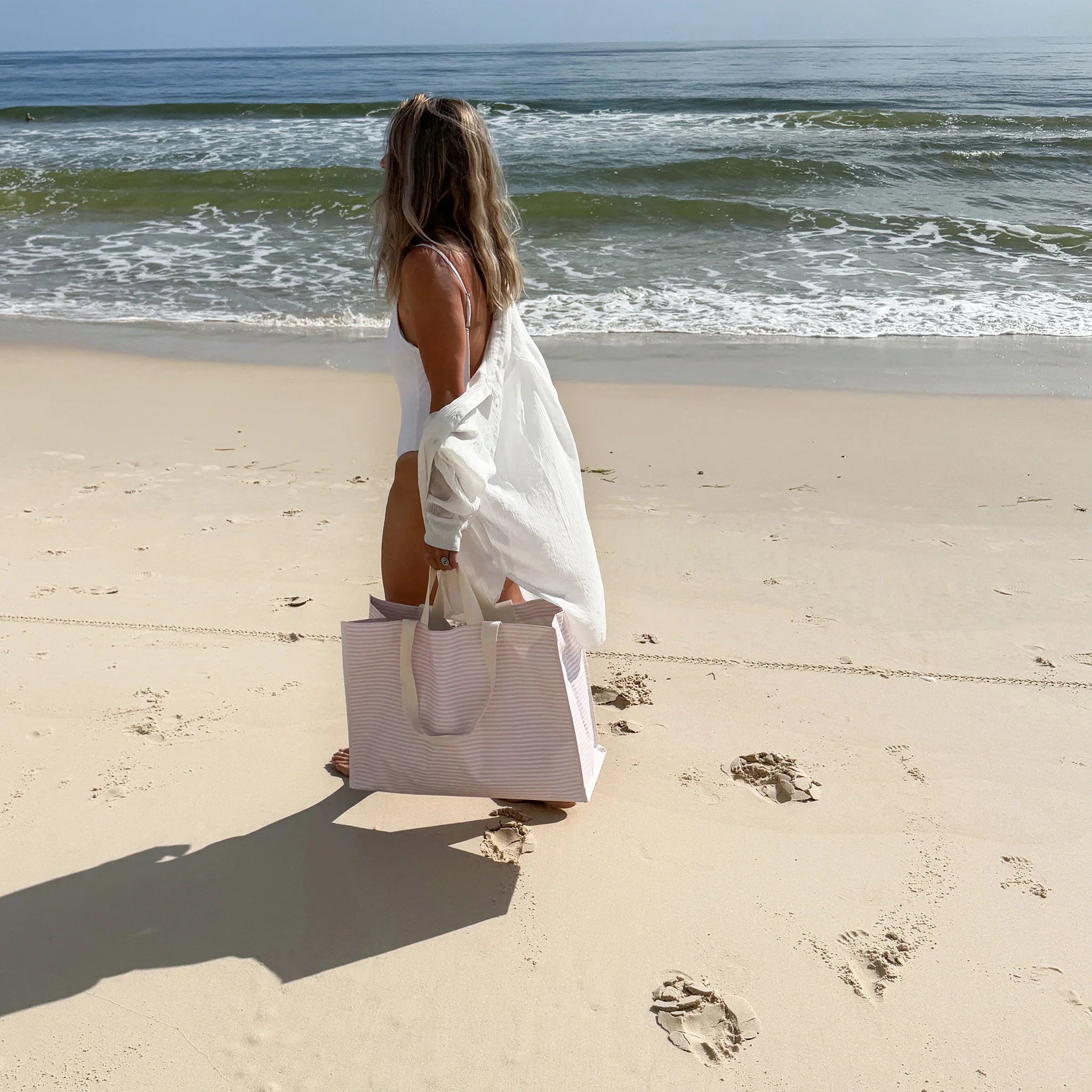 Kobieta trzymająca torba plażowa różowa marki LOQI na piaszczystej plaży przy morzu