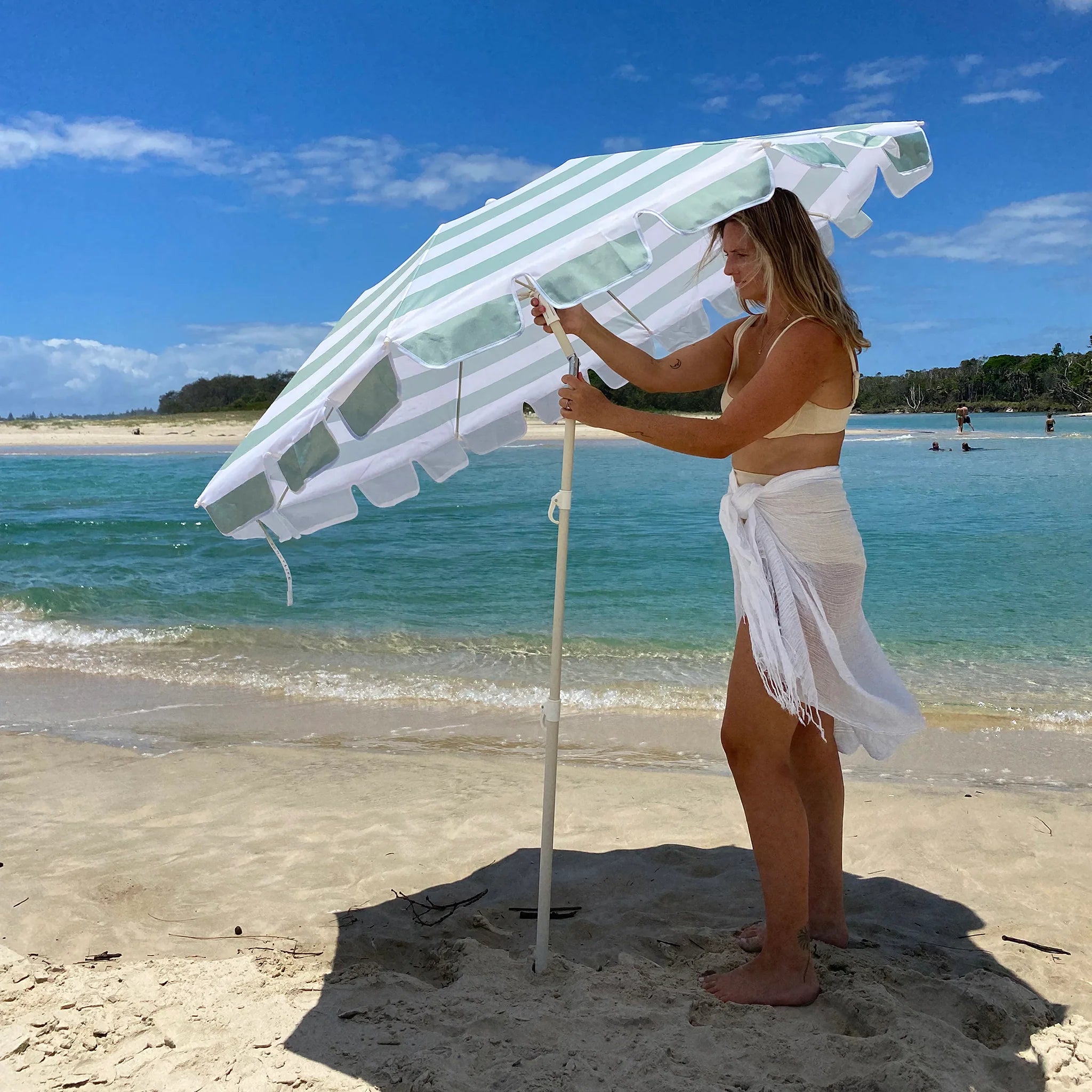 Kompaktowy parasol plażowy LOQI w zielono-białe paski używany na piaszczystej plaży przy słonecznej pogodzie