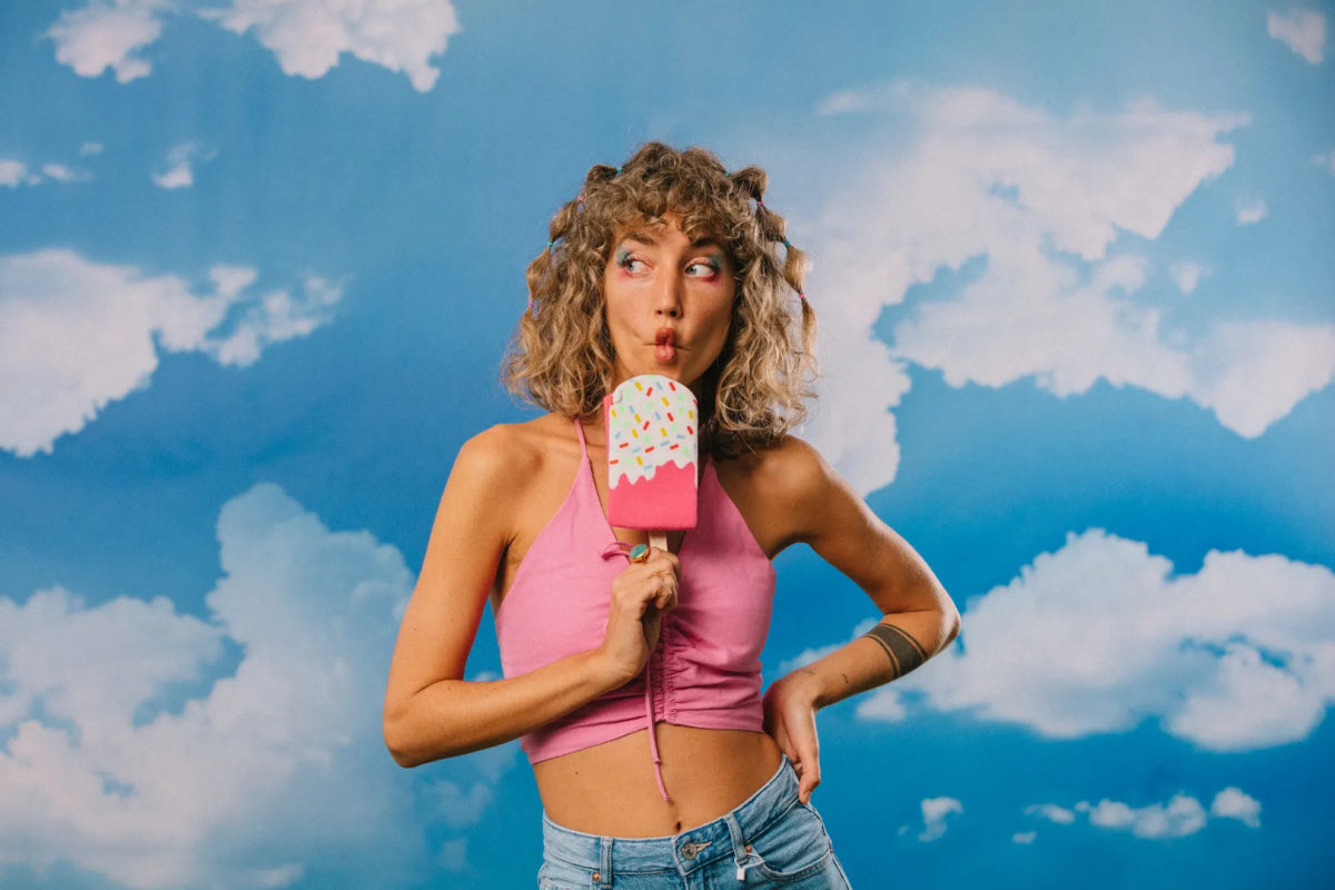 Kobieta w skarpetkach EMS Frozen Pop trzymająca różowe lody na patyku na tle nieba z chmurami