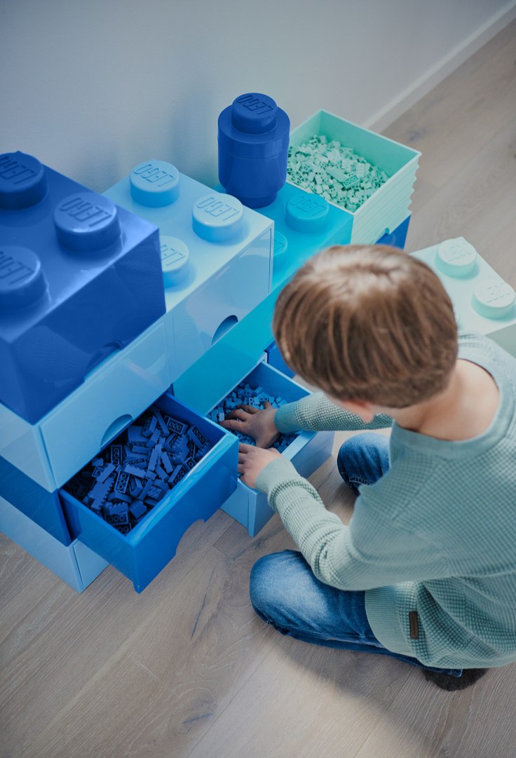 Szuflada LEGO na zabawki w formie dużych klocków z otwartymi pojemnikami i dzieckiem sięgającym po klocki