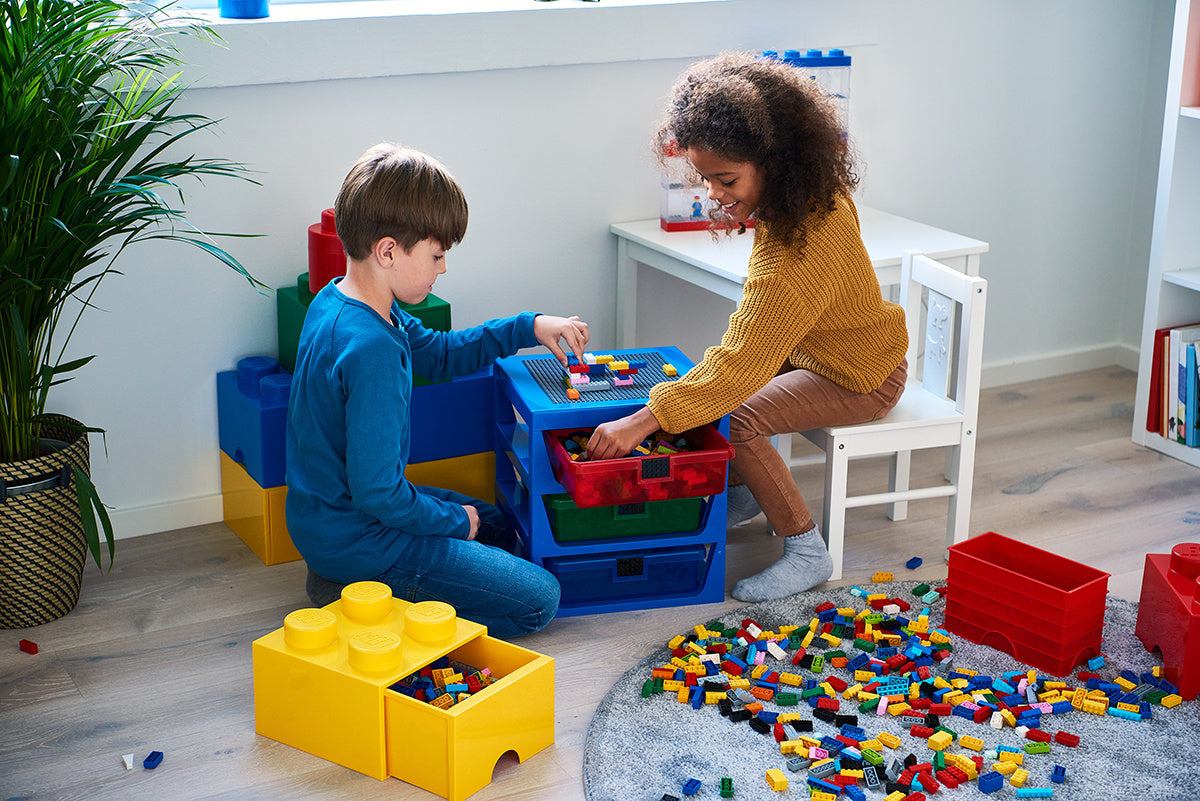 Dwoje dzieci bawi się szufladą klocek LEGO pełną kolorowych elementów w pokoju zabaw