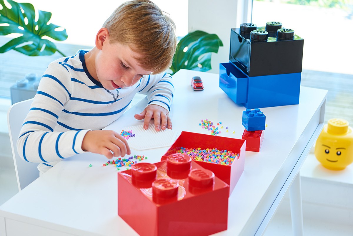 Chłopiec bawiący się koralikami przy biurku z szufladką LEGO na biurko w kształcie klocka