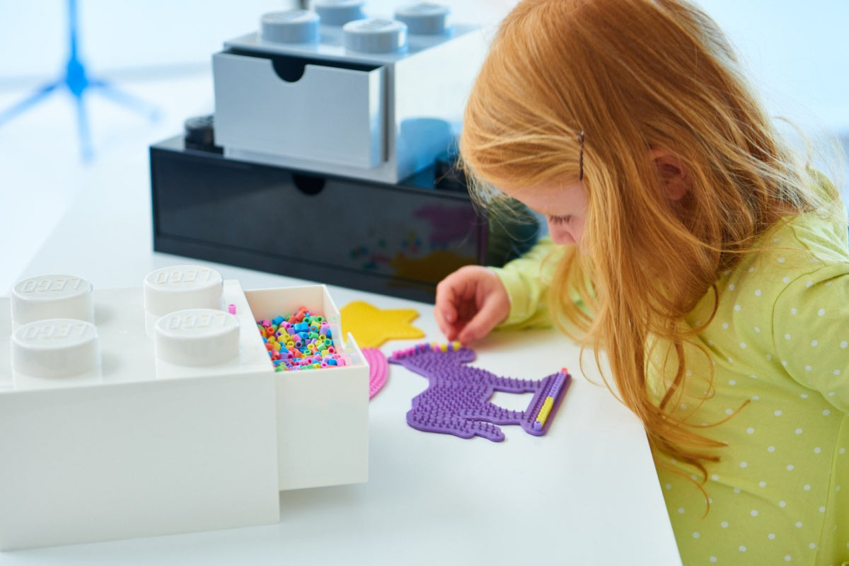 Dziecko bawiące się kreatywnością przy szufladce LEGO na biurko z kolorowymi koralikami i projektami