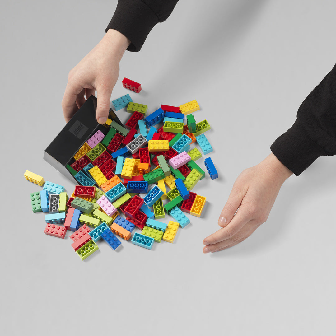 Szufelka do klocków LEGO w czarnym kolorze z kolorowymi klockami i dłońmi osoby sprzątającej