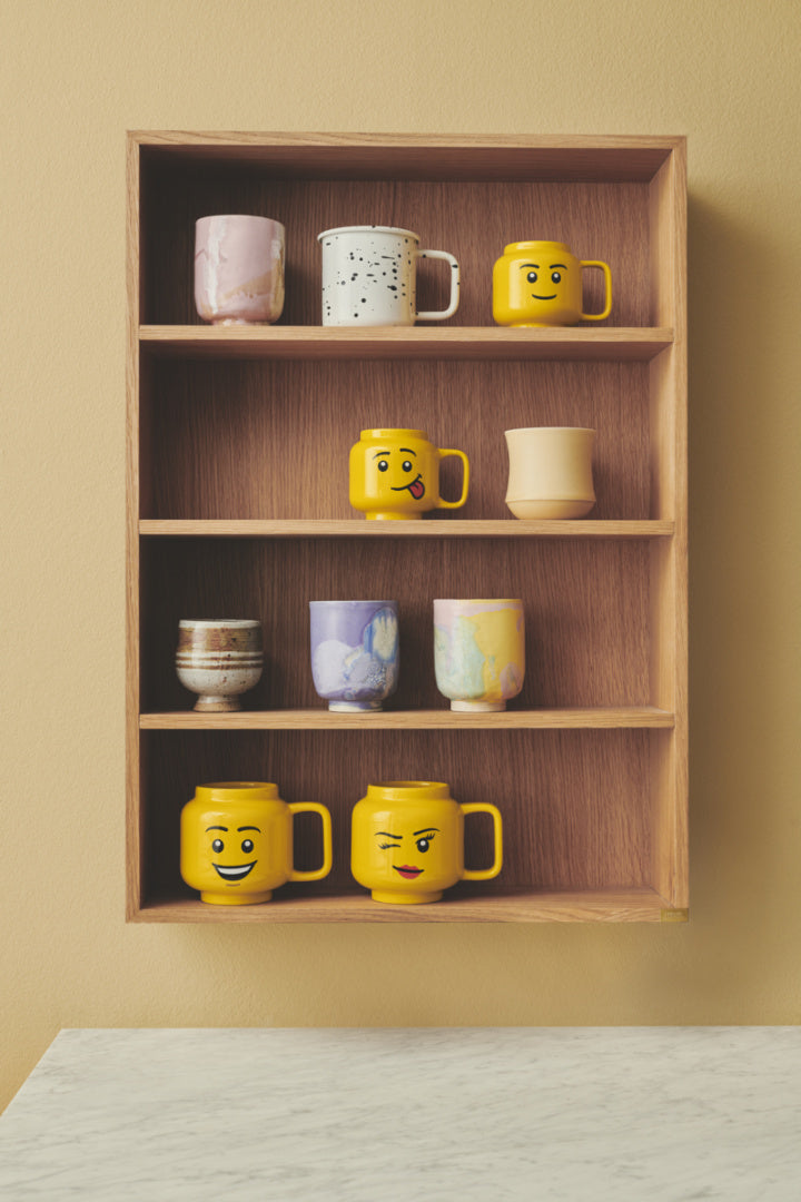 Kubek LEGO głowa ceramiczny w żółtym kolorze z różnymi emotikonami na drewnianej półce