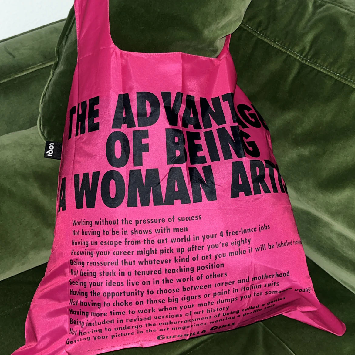 Jasnoróżowa torba LOQI Guerrilla Girls z czarnym nadrukiem tekstowym na zielonej kanapie